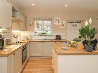 A kitchen with wooden countertops a kitchen island a window and light cabinets at Larch Cottage at Esthwaite Water in Hawkshead