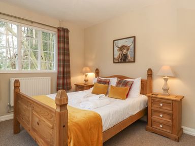 A bedroom with a wooden double bed two bedside tables with lamps and a window with plaid curtains at Larch Cottage at Esthwaite Water in Hawkshead