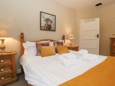 A bedroom with a wooden double bed with white bedding and pillows two bedside tables with lamps and a painting above the bed at Larch Cottage at Esthwaite Water Hawkshead