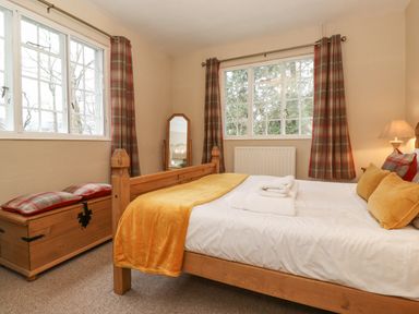 A bedroom with a wooden bed and chest by the window at Larch Cottage at Esthwaite Water in Hawkshead