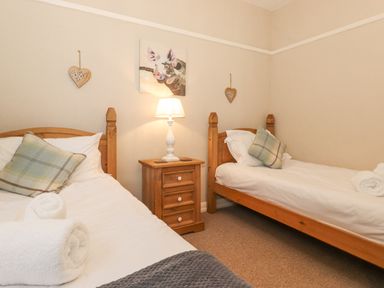 A bedroom with two single wooden beds and a nightstand with a lamp at Larch Cottage at Esthwaite Water in Hawkshead