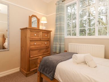 A bedroom with a wooden dresser a bed with towels a window and a mirror at Larch Cottage at Esthwaite Water in Hawkshead