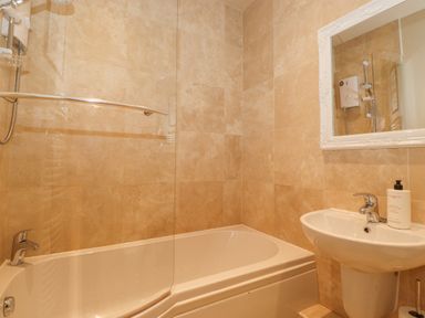 A bathroom with a bathtub shower combination a sink with a faucet and a mirror on the wall at Larch Cottage at Esthwaite Water Hawkshead