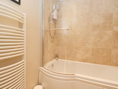 A bathroom with a bathtub and shower with beige tiled walls at Larch Cottage at Esthwaite Water in Hawkshead