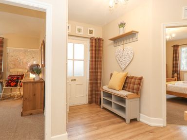 An entryway with a wooden bench with pillows and a wall shelf with hooks and a decorative heart at Larch Cottage at Esthwaite Water Hawkshead