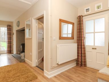An entrance area with a white door and glass panels a radiator a mirror and plaid curtains at Larch Cottage at Esthwaite Water Hawkshead