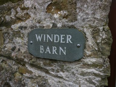 A weathered stone wall with a sign reading Winder Barn at Winder Barn in Askham Cumbria
