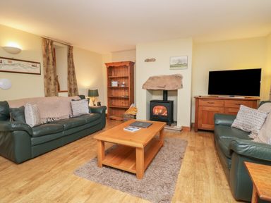 A living room with green leather sofas a wooden coffee table a wood burning stove and a television at Winder Barn in Askham Cumbria