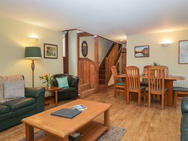A living room with a leather sofa armchair wooden coffee and dining tables and stairs at Winder Barn in Askham Cumbria