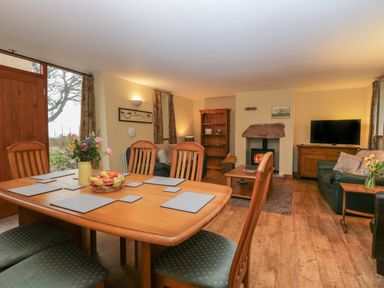 A dining table with chairs and placemats next to a living room with sofas a bookshelf a fireplace and a television at Winder Barn in Askham Cumbria
