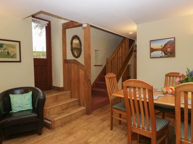 A dining area with wooden table and chairs next to a staircase and a black armchair with a green pillow at Winder Barn in Askham Cumbria