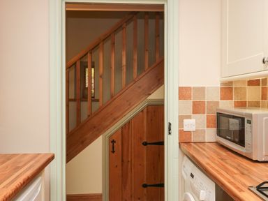 A kitchen with wooden countertops a microwave a washing machine and a wooden door under a staircase at Winder Barn in Askham Cumbria