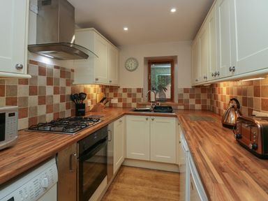 A kitchen with wooden countertops and tiled backsplash with stove microwave kettle and toaster at Winder Barn in Askham Cumbria