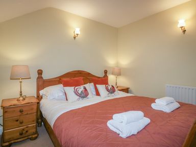 A bedroom with a wooden double bed orange bedspread and pillows bedside tables with lamps and folded towels on the bed at Winder Barn in Askham Cumbria