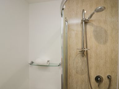 A shower area with a handheld showerhead and a glass shelf holding a folded white towel at Winder Barn in Askham Cumbria