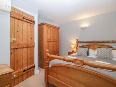 A bedroom with a wooden bed frame wooden wardrobe wooden door and bedside table with lamp at Winder Barn in Askham Cumbria