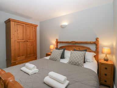 A bedroom with a wooden bed and wardrobe gray bedding and two bedside tables with lamps at Winder Barn in Askham Cumbria