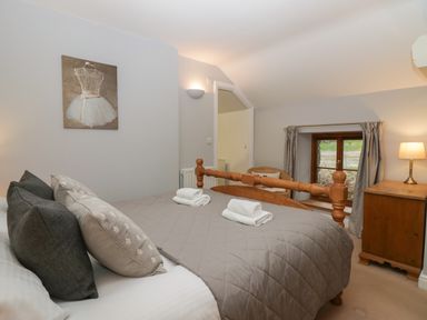 A bedroom with a wooden bed with pillows and folded towels a window with curtains a wooden dresser and a chair at Winder Barn in Askham Cumbria