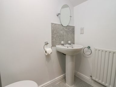 A bathroom with a pedestal sink two taps a round mirror toilet paper holder and a radiator at Winder Barn in Askham Cumbria