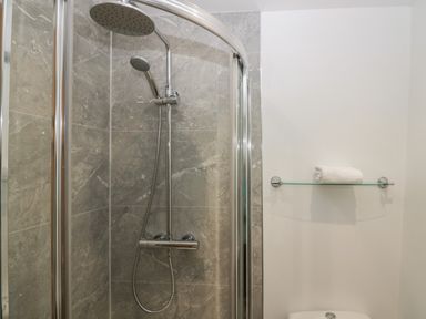 A shower with grey tiled walls a curved glass door and a towel on a glass shelf in a bathroom at Winder Barn in Askham Cumbria