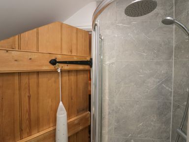 A bathroom with a wooden door and a shower area with gray tiled walls at Winder Barn in Askham Cumbria