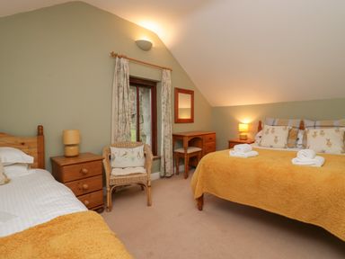 A bedroom with two beds a wooden chair a dresser with a mirror and bedside tables at Winder Barn in Askham Cumbria
