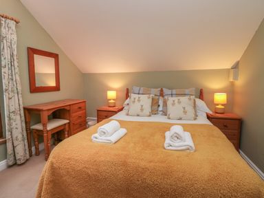 A bedroom with a bed with pillows and folded towels two bedside tables with lamps and a wooden desk with a chair at Winder Barn in Askham Cumbria