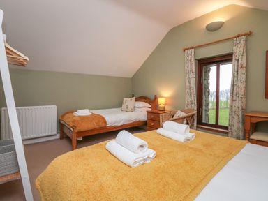 A bedroom with two beds a window with curtains a bedside table with a lamp and a chair at Winder Barn in Askham Cumbria