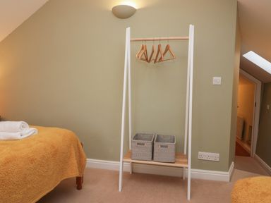 A bedroom corner with a bed with folded towels a white clothes rack with wooden hangers and two gray storage baskets on the lower shelf at Winder Barn in Askham Cumbria