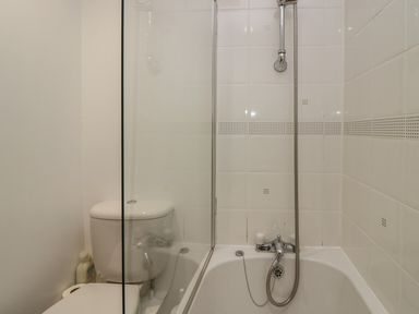 A small bathroom with a toilet, a bathtub with a showerhead, and white tiled walls at Winder Barn in Askham Cumbria