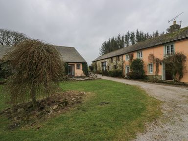 An outdoor scene with a gravel path grass area trees and two stone and peach-colored buildings at Winder Barn in Askham Cumbria