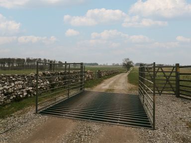 A dirt road with a metal cattle grid gate and stone walls on either side in a rural area at Winder Barn in Askham Cumbria