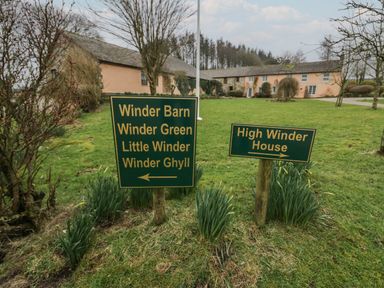 Two green directional signs on grass with buildings and trees in the background at Winder Barn in Askham Cumbria