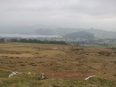 A landscape view of grassy fields with a lake and hills in the background