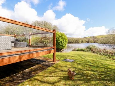 A glass-railed wooden deck with outdoor furniture near a lake with a duck on the grass at Lake View 10 in Par