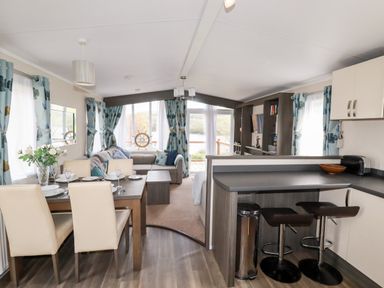 A dining area with table and chairs next to a kitchen counter with stools and a living room with sofa and curtains at Lake View 10 in Par