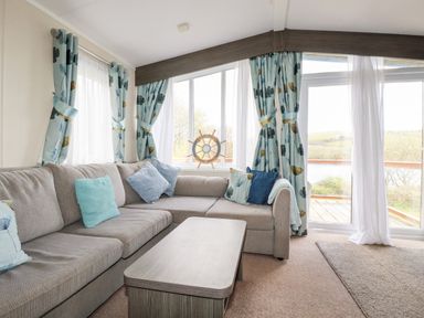 A living room with a gray sectional sofa and a wooden coffee table next to large windows with blue patterned curtains at Lake View 10 in Par