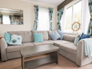 A corner sofa with cushions next to windows with curtains and a wooden coffee table at Lake View 10 in Par