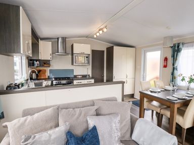 A kitchen with appliances and cabinets next to a dining table set with plates and glasses and a sofa with cushions at Lake View 10 in Par