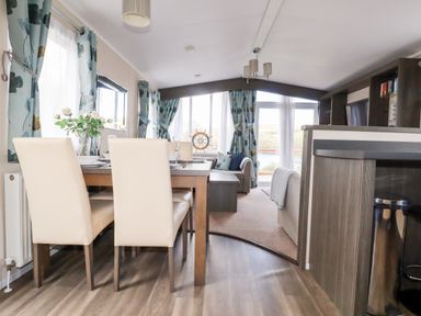 A dining area with a wooden table and cream chairs next to a living room with a sofa a coffee table and windows with blue patterned curtains at Lake View 10 in Par