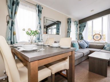 A dining table set with bowls and glasses next to a sofa with cushions and windows with curtains at Lake View 10 in Par