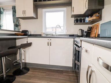 A kitchen with white cabinets a window a sink a stove two black bar stools and kitchen utensils at Lake View 10 in Par
