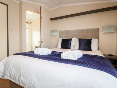 A bedroom with a double bed made with white sheets and blue pillows and blanket with rolled towels on the bed at Lake View 10 in Par