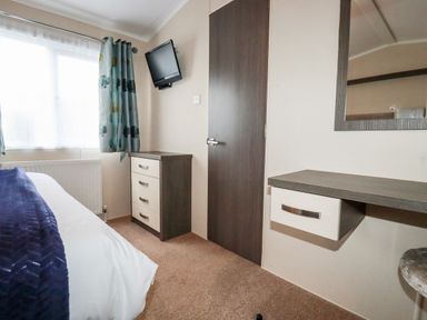 A bedroom with a bed a window with curtains a chest of drawers a wall mounted television a door a wall mirror and a floating desk at Lake View 10 in Par