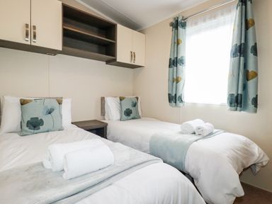 A bedroom with two single beds with floral cushions and rolled towels under a window with matching curtains at Lake View 10 in Par
