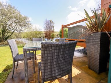 An outdoor patio with a glass top table and four woven chairs near a grassy area and plants at Lake View 10 in Par