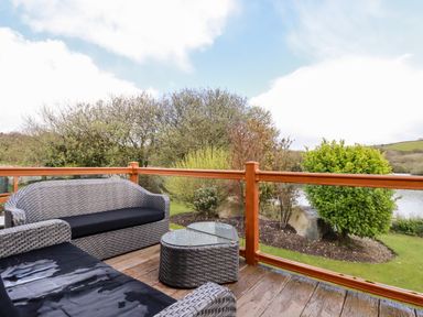 An outdoor deck with wicker furniture and a glass table overlooking a garden and body of water at Lake View 10 in Par
