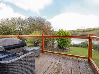 An outdoor deck with wicker chairs and a glass table overlooking a garden and a body of water at Lake View 10 in Par