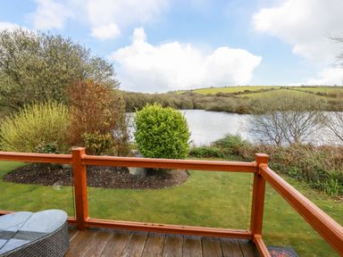 A wooden deck with a glass railing overlooking a grassy garden with shrubs and a lake in the background at Lake View 10 in Par