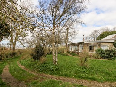 A gravel driveway beside a stone house with large windows and leafless trees on a grassy area at Eweleaze in West Bexington